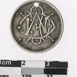 Round silver coloured medal with intertwined stylized letters.