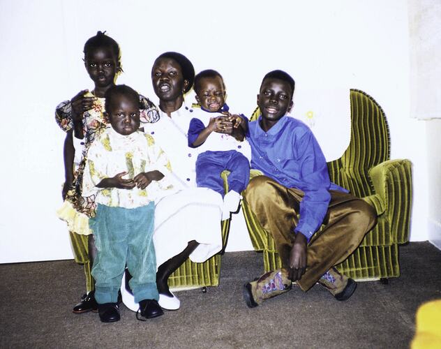 Woman sits on green velvet chair with four children. The eldest boy sits beside her on a second chair.