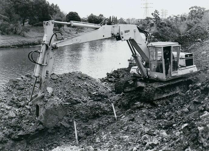Man operating a Crawler Excavator beside a river.