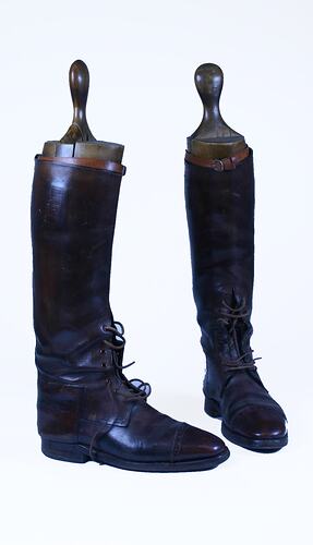Pair of knee-high brown leather boots, laced at the ankles, with wooden boot shapers inserted.