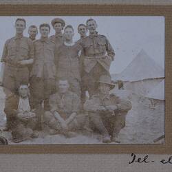 Group of servicemen in a camp with tents behind them.