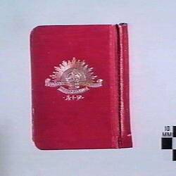 Red book with white Rising Sun emblem in centre, back view.