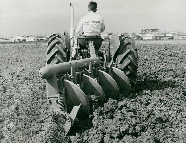 Rear view of  a man driving a tractor with a disc plough attached in a field.