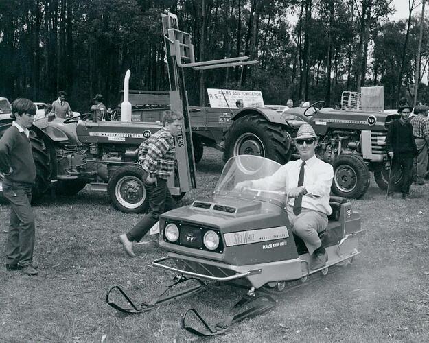 Two youths are looking at a man sitting on a snowmobile.