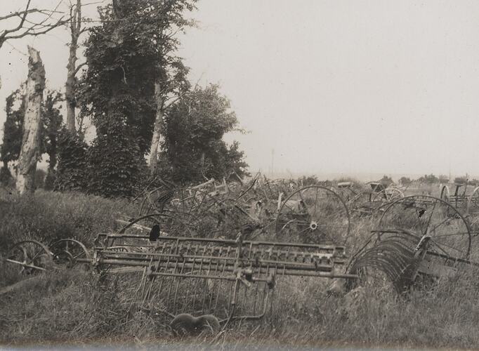 Deserted agricultural machinery located in an overgrown, grassy field with several trees nearby.
