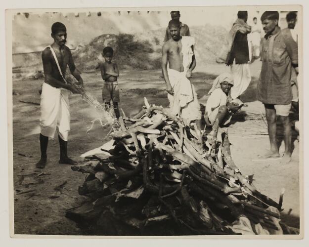 Group of men surrounding a pile small logs of wood.