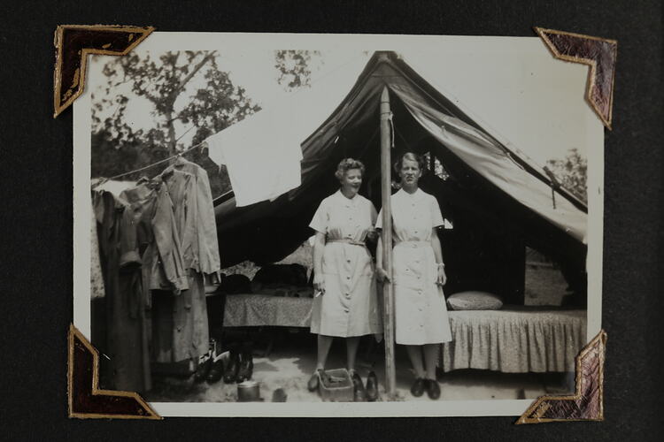 Two women standing in front of a tent, clothes hanging from rope attached to tent.
