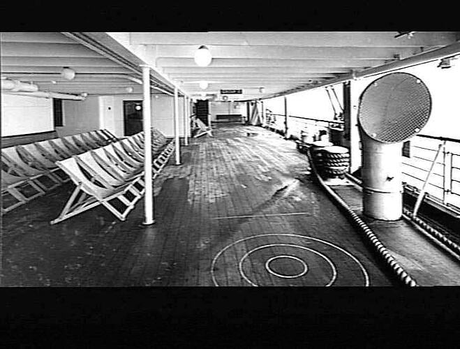 Onboard a ship. Decked area with deck chairs at left, promenade at right.