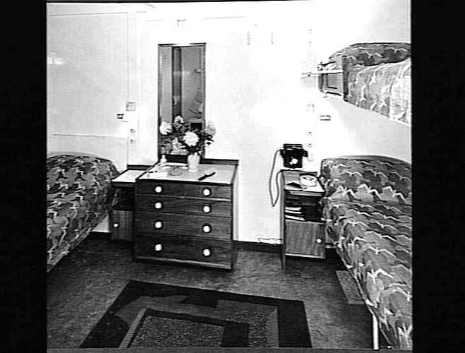 Ship interior. Bed on left, bunk beds on right. Chest of drawers in centre.