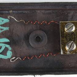 Rectangular dark photocell, open in half. This half has two spiral wires attached to inside wall via metal pla