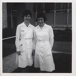 Two smiling women in white factory uniforms.