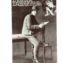 Front of postcard with soldier on table reading.
