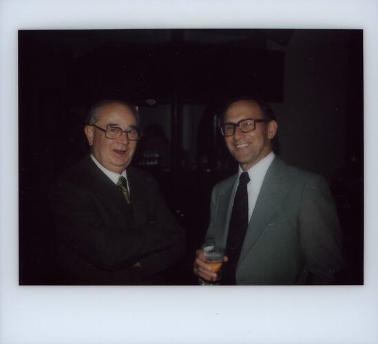 Two men in suits, one with a beer.