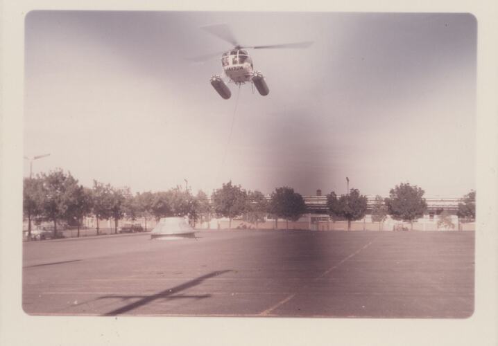 Chimney lid on ground, chained to hovering helicopter.
