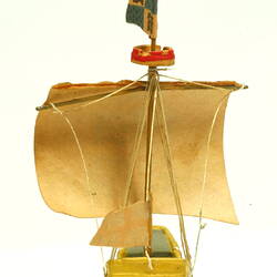 Rear view of ship with yellow hull and painted sail.