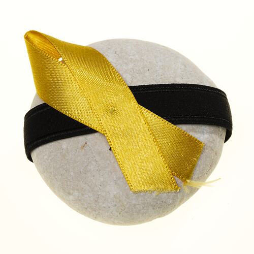 Round pale grey river stone with black band featuring folded yellow ribbon.