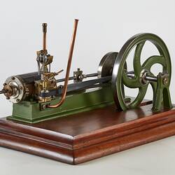 Metal model with large wheel and piston. Green painted frame, wooden base.