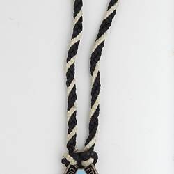 Triangular medal with magpie and black, blue and brown enamel. Black and white twined cord. Silver text.