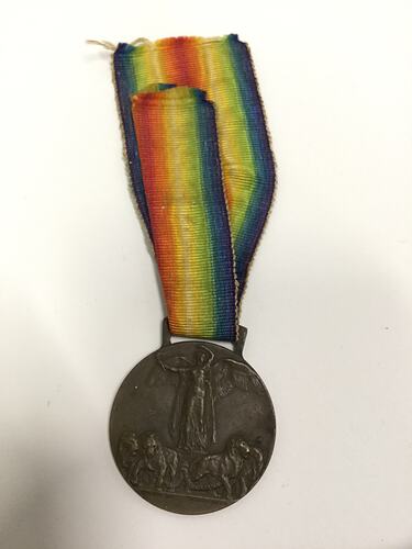 Round dark medal with rainbow-coloured striped ribbon.