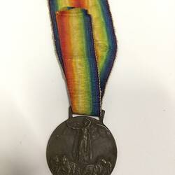 Round dark medal with rainbow-coloured striped ribbon.