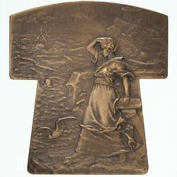 Bronze tau (t-shaped) medal, woman looking out to a rough sea at a shipwreck.