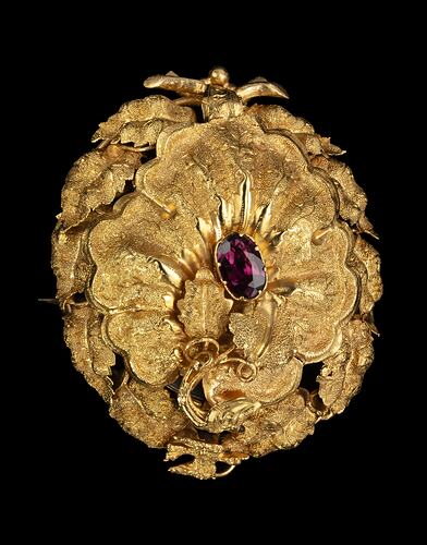 Gold oval locket brooch. Vine leaves and tendrils border. Branches at base with a small bird at top, all supporting a large flower with an amethyst purple paste stone centre.