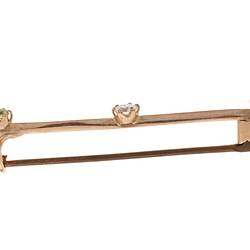 Profile of gold bar brooch with three gemstones. Purple amethyst at left end, diamond in centre and light green peridot at right end.
