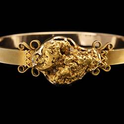 Gold bangle (bracelet) featuring a large gold nugget. Chain hanging at right.
