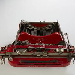 Red metal typewriter, 32 keys, black plastic spacebar at front, black roller for paper at top back. Top view