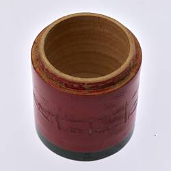 Open red painted, cylindrical wooden box. Dark green trim around base.