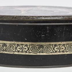 Side view of round black metal tin with lid. Central decorative gold band.