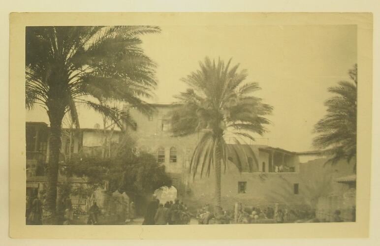 Village scene with buildings, palm trees and people.