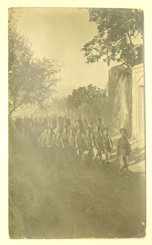 Military men wearing turbans marching down walled street.