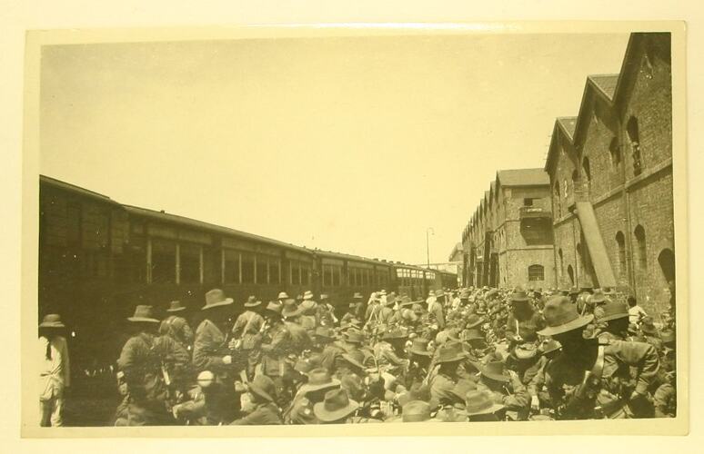 Crowd of soldiers on platform between train and buildings.