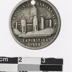 Round silver coloured medal with building and text surrounding.