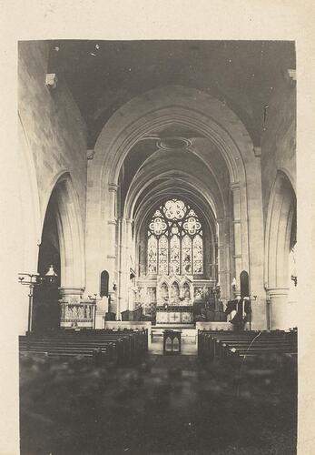 Church interior with rows of pews and altar and stained glass window in centre.