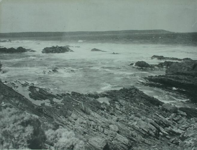 Seascape image with land fall point in the distance. Rocky coastal foreground.
