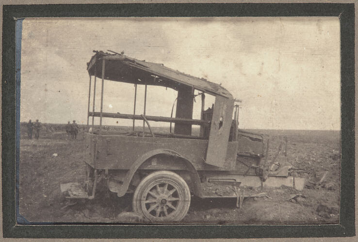 Destroyed shell of a truck with servicemen on in the background on the right.