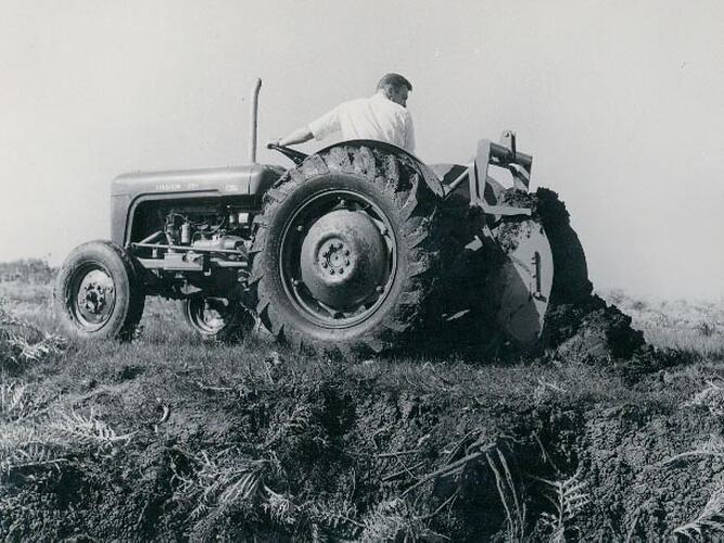 Side view of a man driving a tractor coupled to an earth scoop.