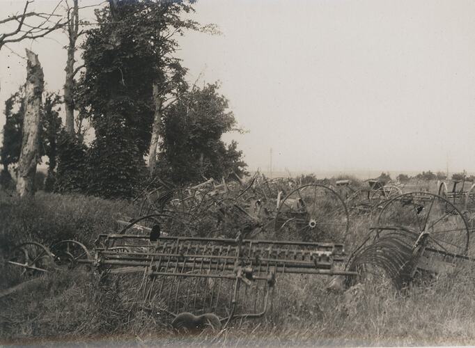 Deserted agricultural machinery located in an overgrown, grassy field with several trees nearby.