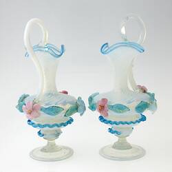 Pair of blue blown-glass ewer, spiral fluted neck, serpentine handle, flattened bulbous body layered with pink, blue, green flowers and leaves.