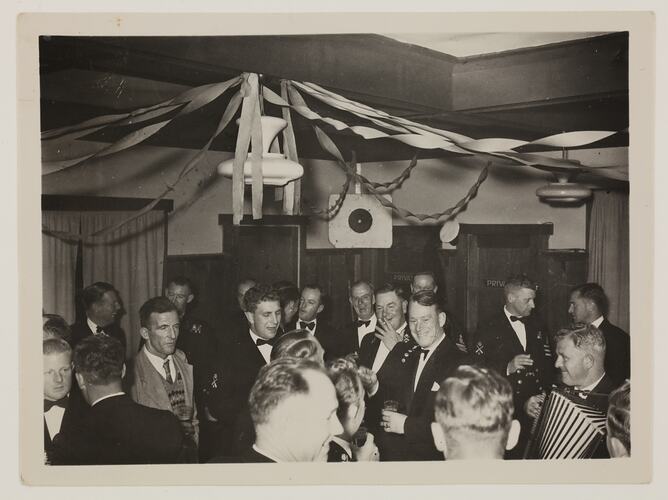 Group of men in suits, standing under a light with streamers attached.