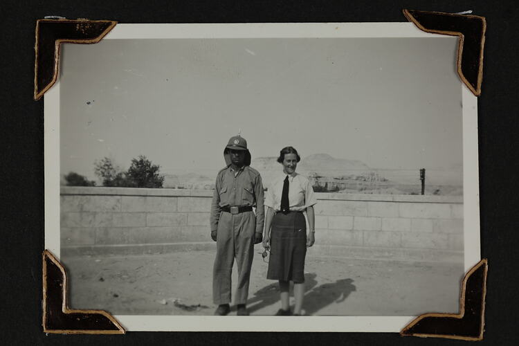 Man and woman in uniform standing in front of waste height stone wall.