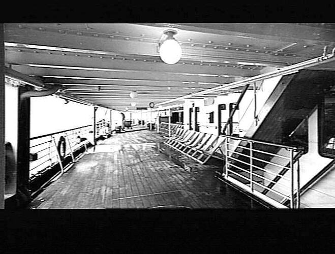 Onboard a ship. Decked area with staircase at right, promenade at left.