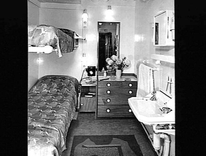 Ship interior. Bunk beds on left, handbasin on right. Chest of drawers in centre.