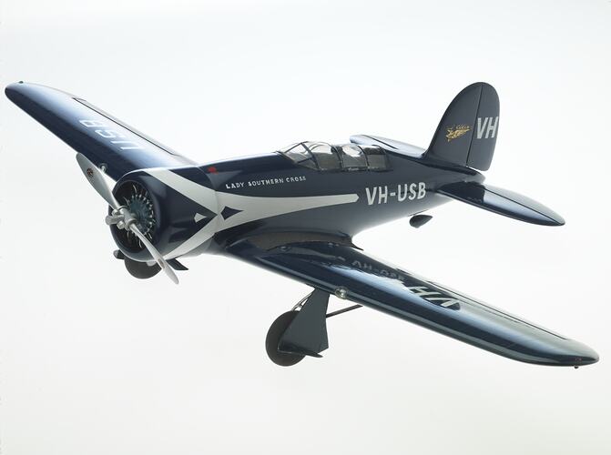 Metal dark blue model aeroplane with white stripe. Cockpit on top of body, silver propeller at front.