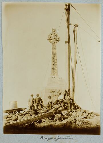 Five men posed front of stone monument surrounded by construction material.