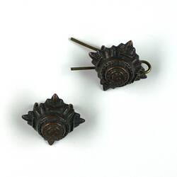 Pair of cast metal pips, bronze colour, square shape with circular motif within.