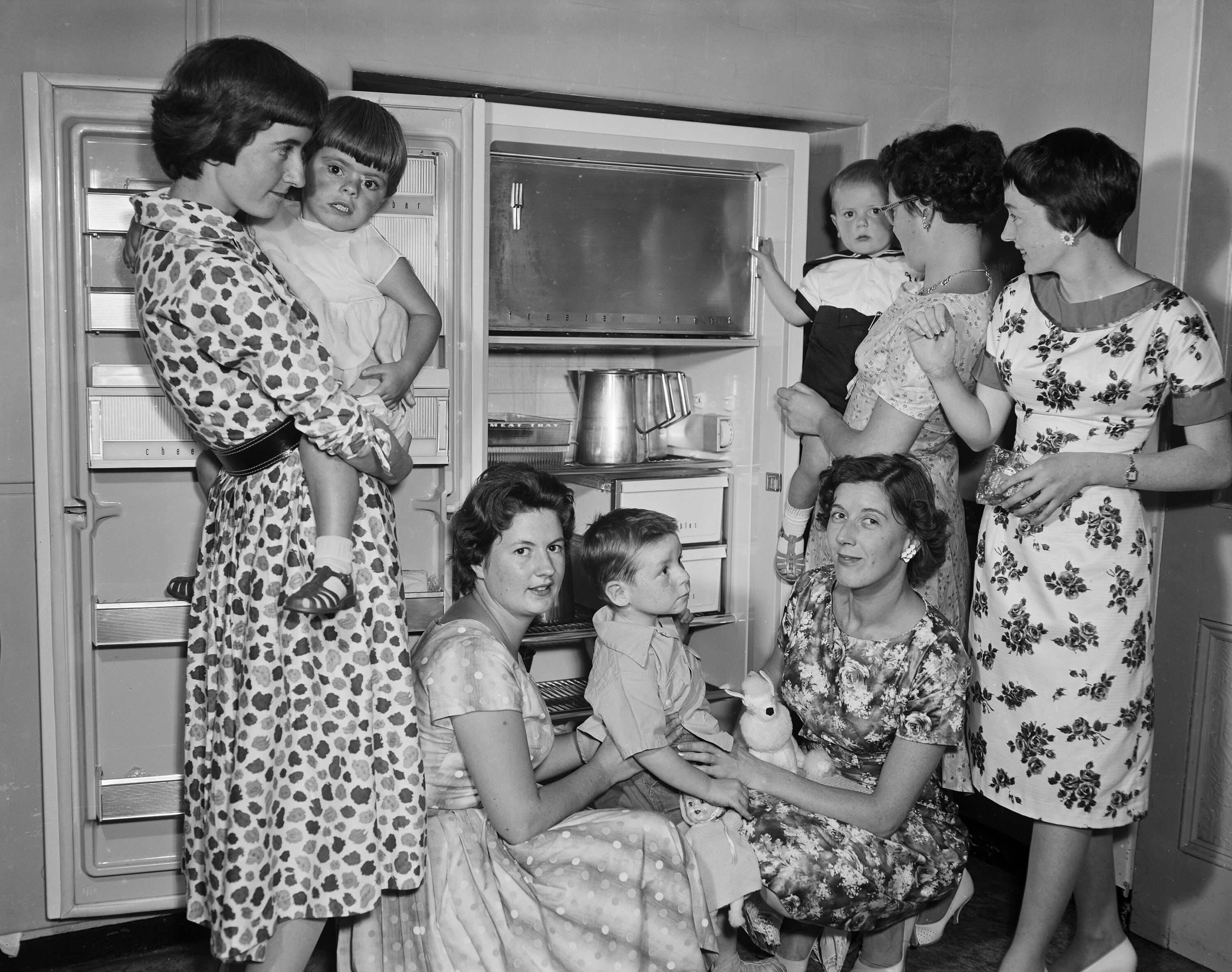 A group of women and children stand beside a large refrigerator in a textile shop.