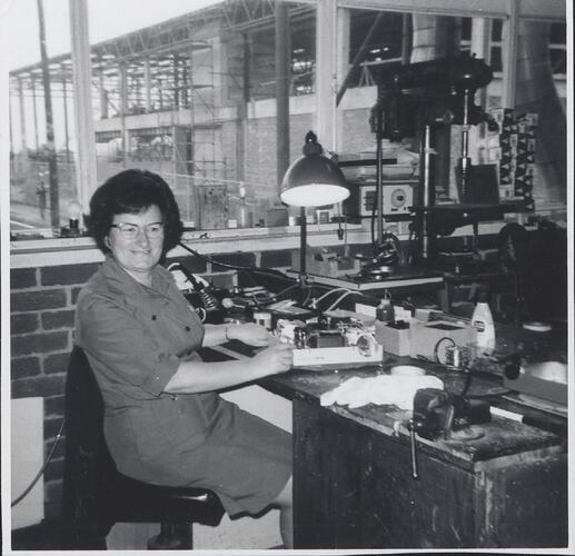 Woman seated at workbench.